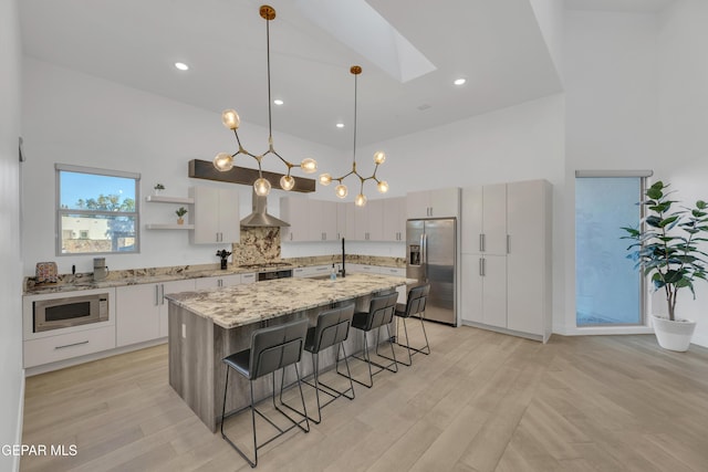 kitchen with wall chimney range hood, open shelves, a breakfast bar, stainless steel appliances, and a towering ceiling