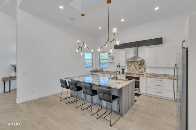 kitchen featuring wall chimney range hood, light wood finished floors, stainless steel appliances, white cabinetry, and decorative backsplash