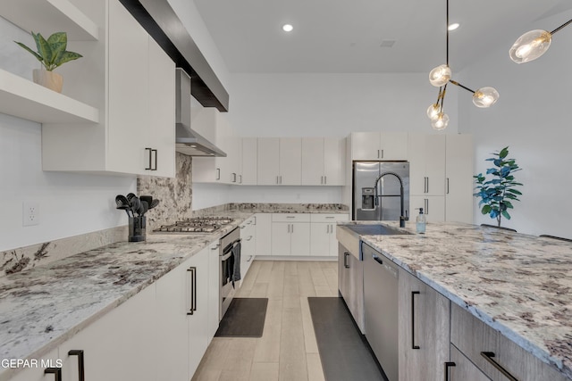 kitchen with wall chimney range hood, light stone countertops, appliances with stainless steel finishes, a sink, and light wood finished floors
