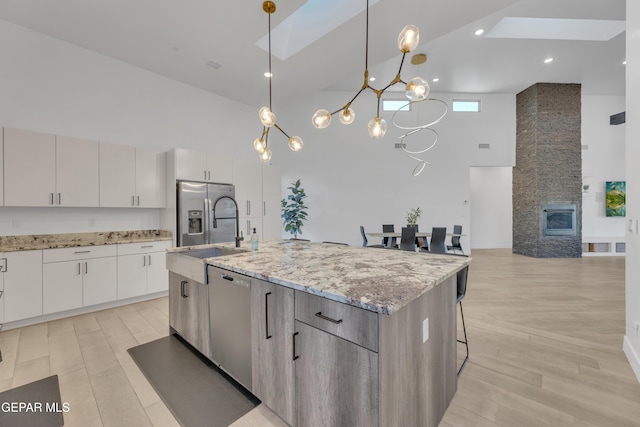 kitchen featuring appliances with stainless steel finishes, light stone countertops, a center island with sink, a sink, and high vaulted ceiling