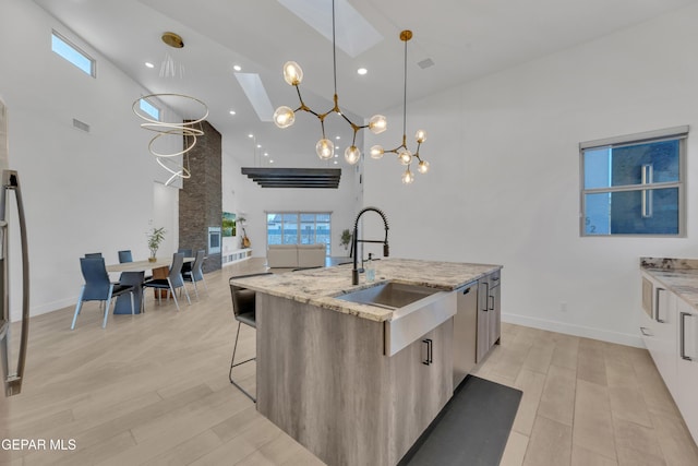 kitchen with light stone counters, a sink, light wood-style flooring, and high vaulted ceiling