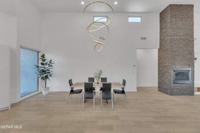 dining room featuring a high ceiling, visible vents, a stone fireplace, and wood finished floors