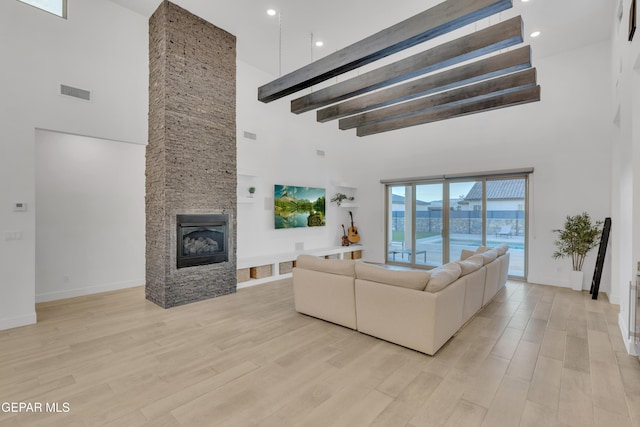 living area with a fireplace, light wood-style flooring, baseboards, a towering ceiling, and visible vents
