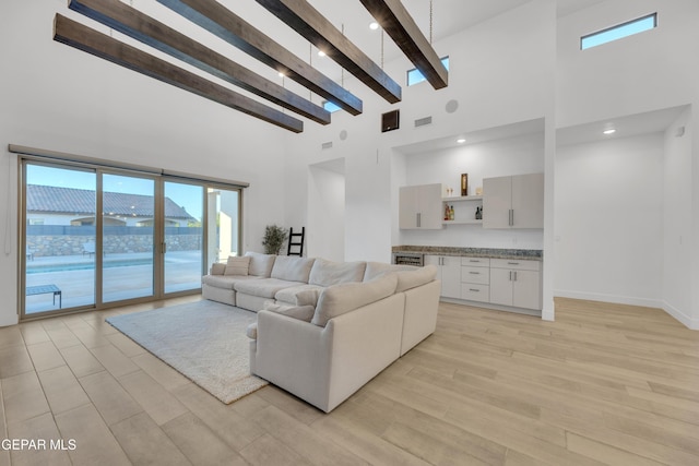 living area with visible vents, beam ceiling, baseboards, a high ceiling, and light wood-style flooring