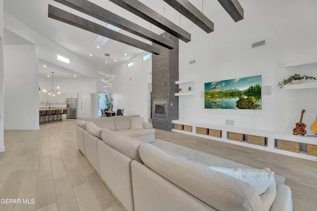living room with beamed ceiling, light wood-style floors, a stone fireplace, high vaulted ceiling, and a notable chandelier
