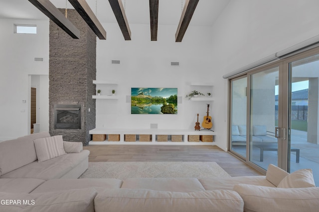 living area with beam ceiling, visible vents, wood finished floors, and a towering ceiling