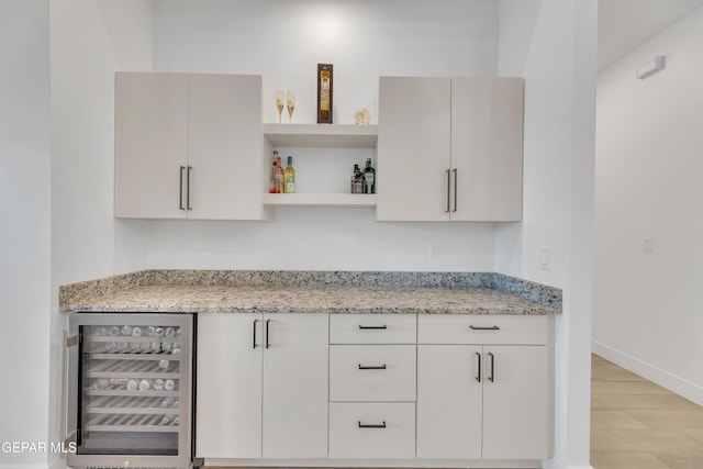 kitchen with beverage cooler, open shelves, light wood finished floors, and light stone counters