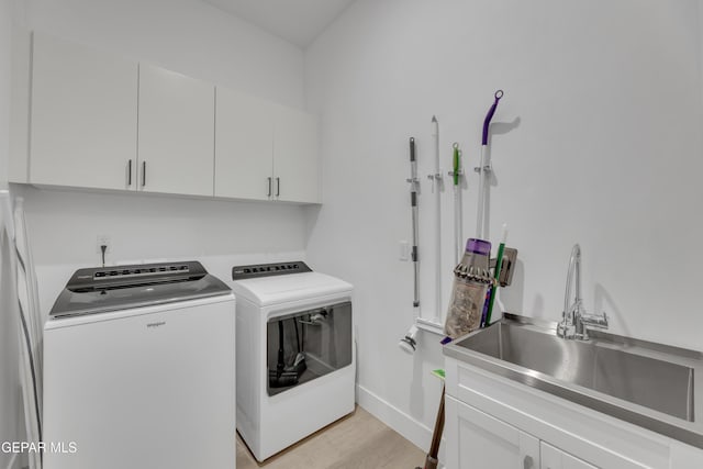 washroom with baseboards, separate washer and dryer, a sink, cabinet space, and light wood finished floors