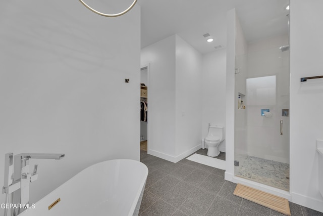 bathroom with a walk in closet, a freestanding tub, a walk in shower, baseboards, and toilet