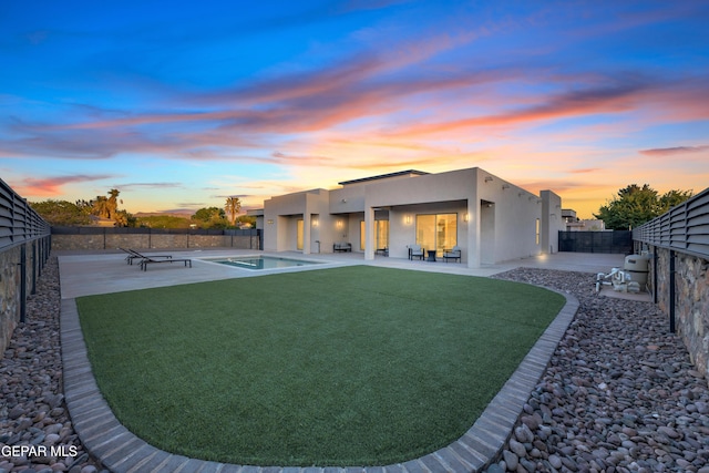 back of property at dusk featuring stucco siding, a fenced backyard, a fenced in pool, a patio area, and a lawn