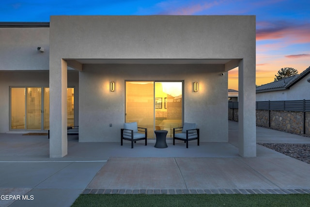 back of property at dusk featuring a patio, stucco siding, and fence