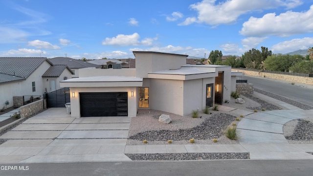 contemporary home with concrete driveway, an attached garage, fence, and stucco siding