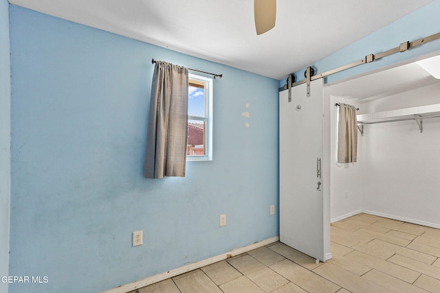 empty room with baseboards, a barn door, and ceiling fan