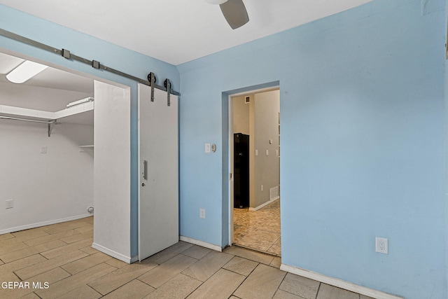 unfurnished bedroom with a barn door, a closet, a ceiling fan, visible vents, and baseboards