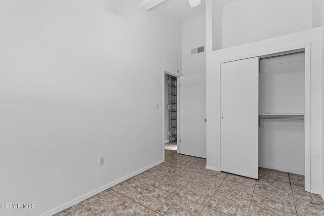 unfurnished bedroom featuring tile patterned floors, a closet, baseboards, visible vents, and a high ceiling