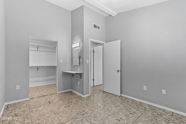 unfurnished bedroom with visible vents, a closet, a spacious closet, tile patterned flooring, and a high ceiling