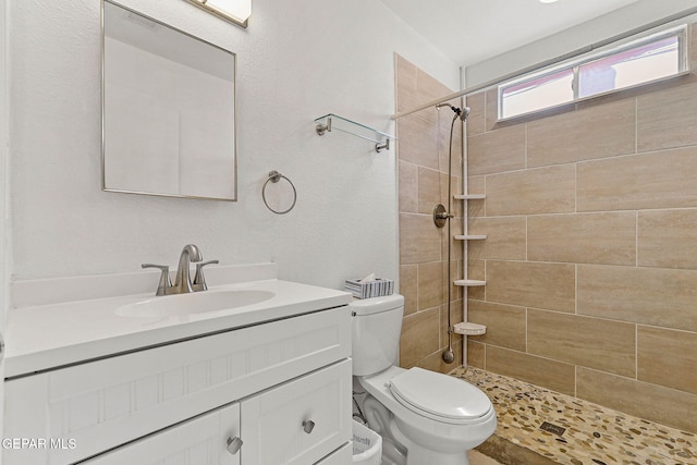 bathroom featuring toilet, a tile shower, and vanity