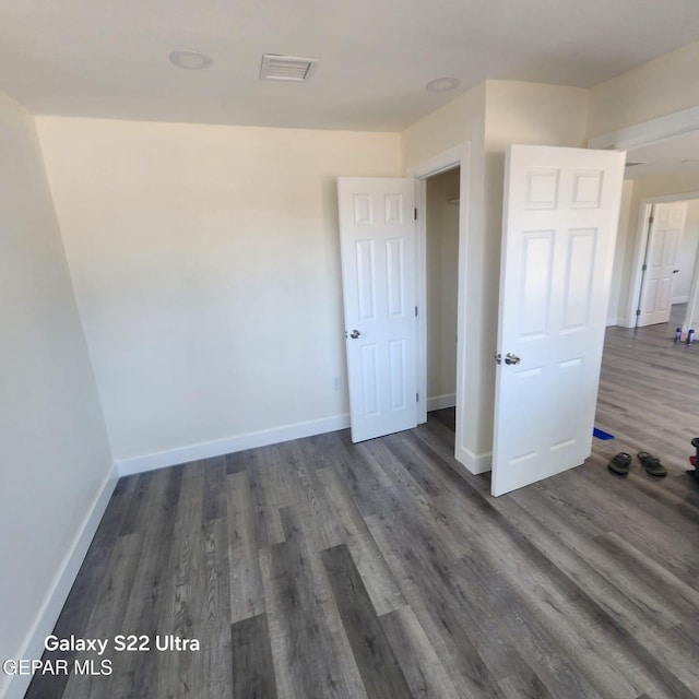 spare room featuring dark wood-type flooring, visible vents, and baseboards