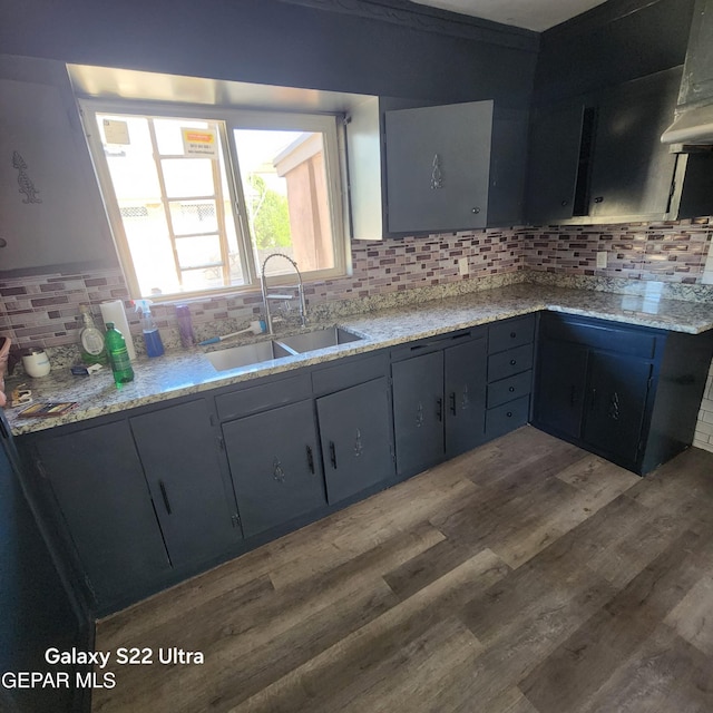 kitchen with range hood, light stone counters, wood finished floors, a sink, and tasteful backsplash