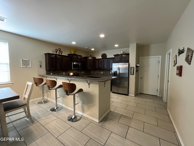 14700 Alton Oaks, El Paso, TX 79938 - kitchen with dark brown cabinetry, a kitchen bar, a peninsula, stainless steel appliances, and recessed lighting