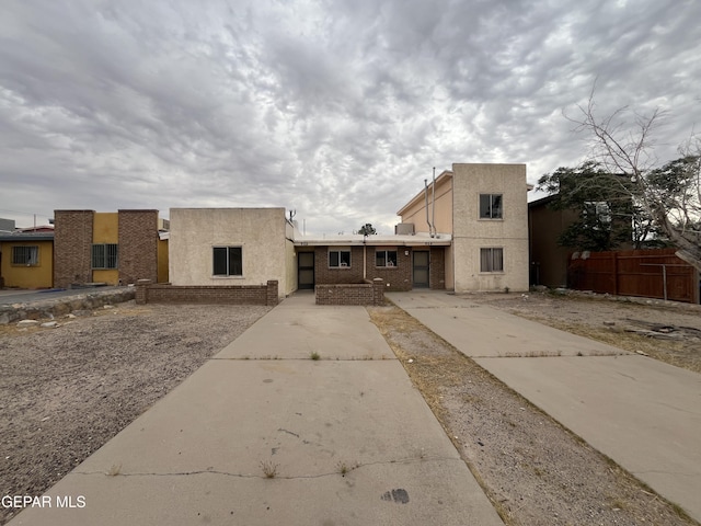 view of front of property with stucco siding, driveway, brick siding, and fence