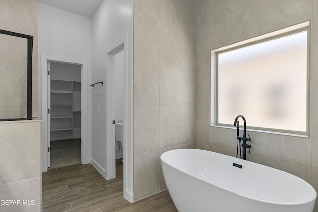 3780 Surmise St, El Paso, TX 79938 - bathroom featuring wood finished floors, a freestanding bath, a spacious closet, tile walls, and toilet