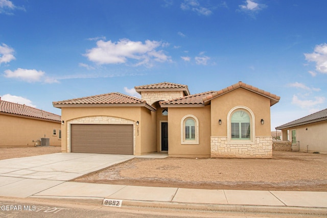 mediterranean / spanish-style house with stone siding, cooling unit, stucco siding, concrete driveway, and an attached garage