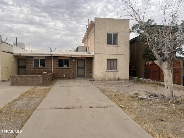 view of front of property featuring stucco siding, fence, a patio, and brick siding