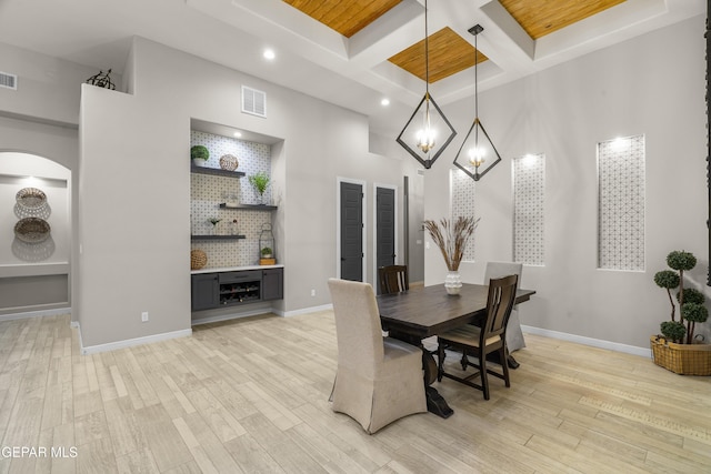 dining area with light wood finished floors, a chandelier, a towering ceiling, visible vents, and coffered ceiling