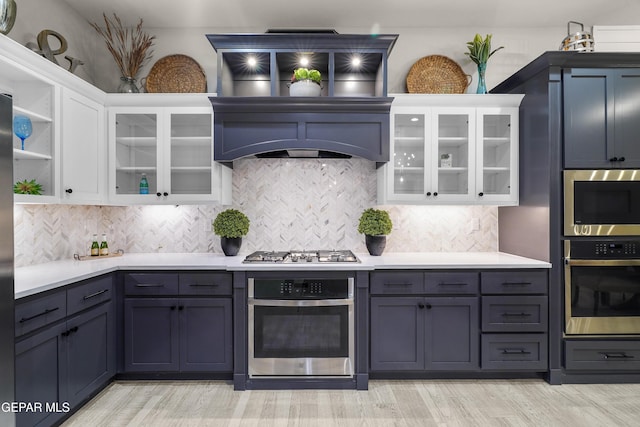 kitchen with appliances with stainless steel finishes, tasteful backsplash, light countertops, white cabinets, and light wood-style flooring