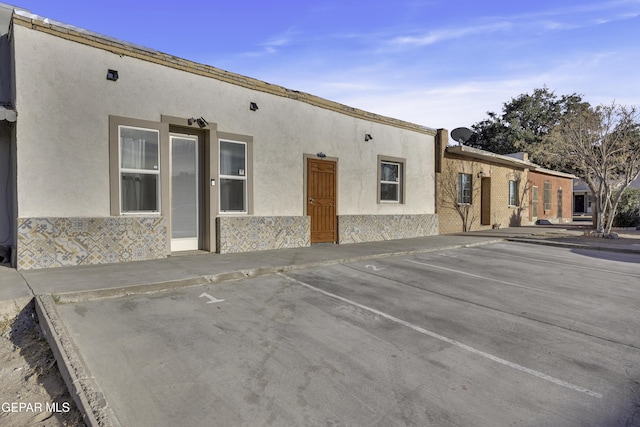 exterior space with stone siding, uncovered parking, and stucco siding