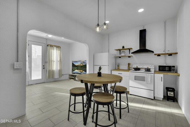 kitchen featuring white cabinets, open shelves, white appliances, arched walkways, and wall chimney exhaust hood