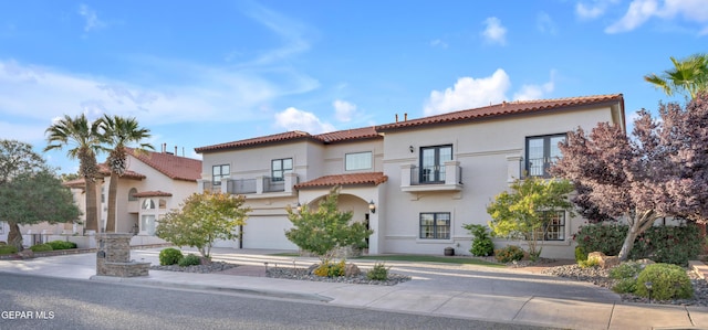 mediterranean / spanish house with a tiled roof, an attached garage, stucco siding, and a balcony