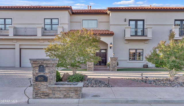 view of front facade with a tile roof, a garage, decorative driveway, a balcony, and stucco siding