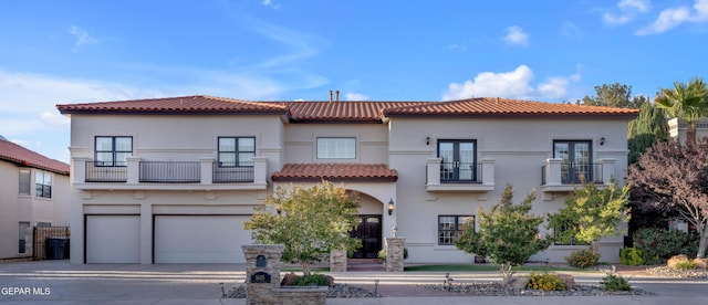 mediterranean / spanish home featuring french doors, a tile roof, a balcony, concrete driveway, and stucco siding