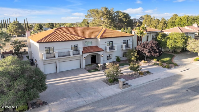 mediterranean / spanish house with driveway, a tile roof, a balcony, an attached garage, and stucco siding