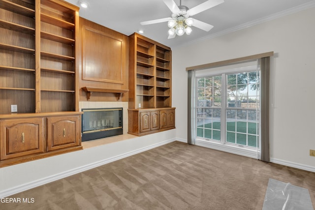 unfurnished living room featuring ceiling fan, baseboards, a glass covered fireplace, ornamental molding, and carpet