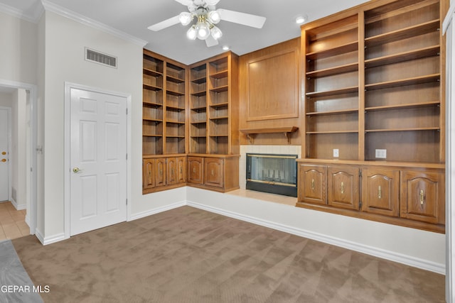 unfurnished living room with visible vents, crown molding, built in features, dark carpet, and a ceiling fan