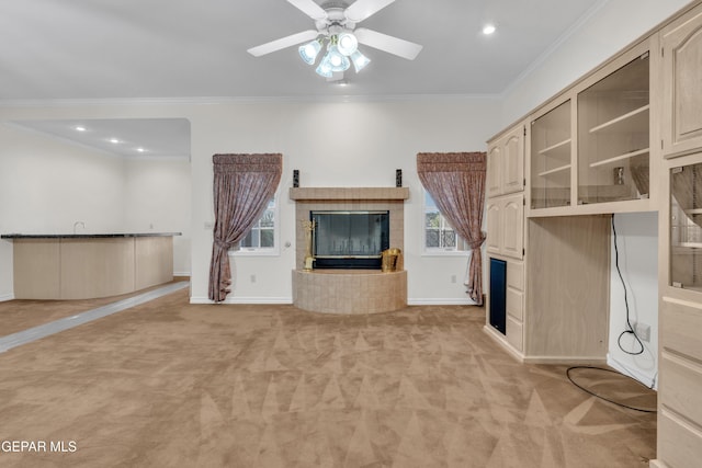 unfurnished living room featuring crown molding, ceiling fan, light carpet, a fireplace, and baseboards