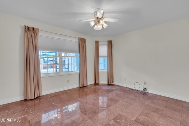 spare room featuring baseboards, a ceiling fan, marble finish floor, and a healthy amount of sunlight