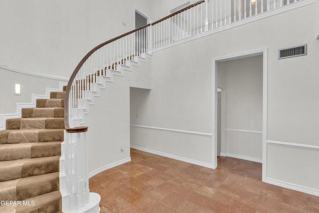 staircase with a towering ceiling, baseboards, and visible vents