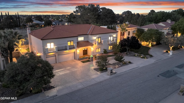 mediterranean / spanish home featuring an attached garage, stucco siding, a balcony, a tiled roof, and driveway
