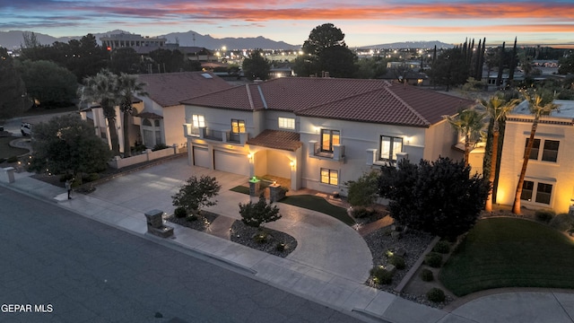 mediterranean / spanish-style home with a tiled roof, curved driveway, a balcony, an attached garage, and stucco siding