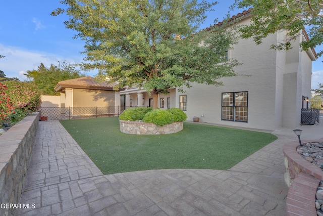 view of front facade featuring a tile roof, a front yard, fence, a patio, and stucco siding