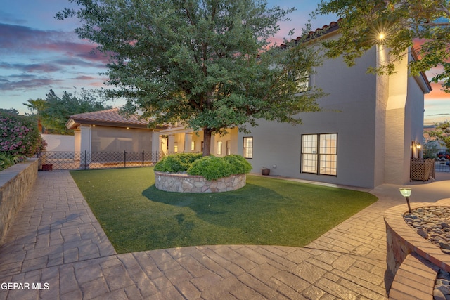 rear view of property featuring a yard, a tiled roof, fence, and stucco siding