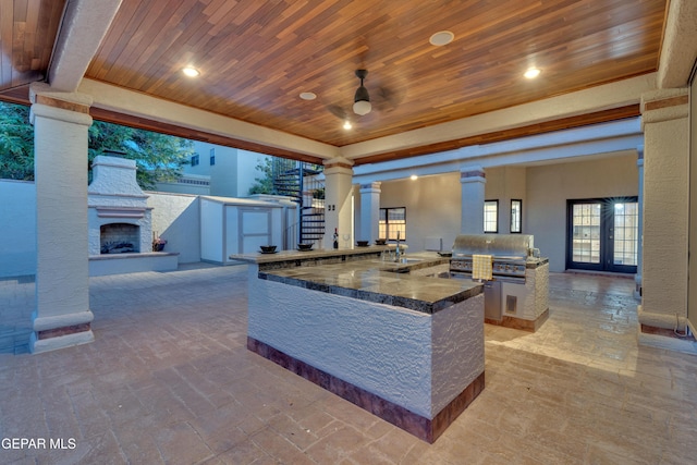 kitchen featuring wood ceiling, a ceiling fan, an outdoor stone fireplace, a peninsula, and ornate columns