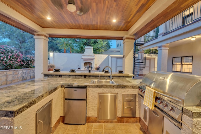 view of patio with grilling area, an outdoor fireplace, exterior kitchen, a sink, and stairs