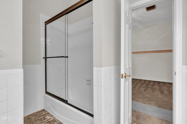 full bath with visible vents, enclosed tub / shower combo, a wainscoted wall, and tile walls
