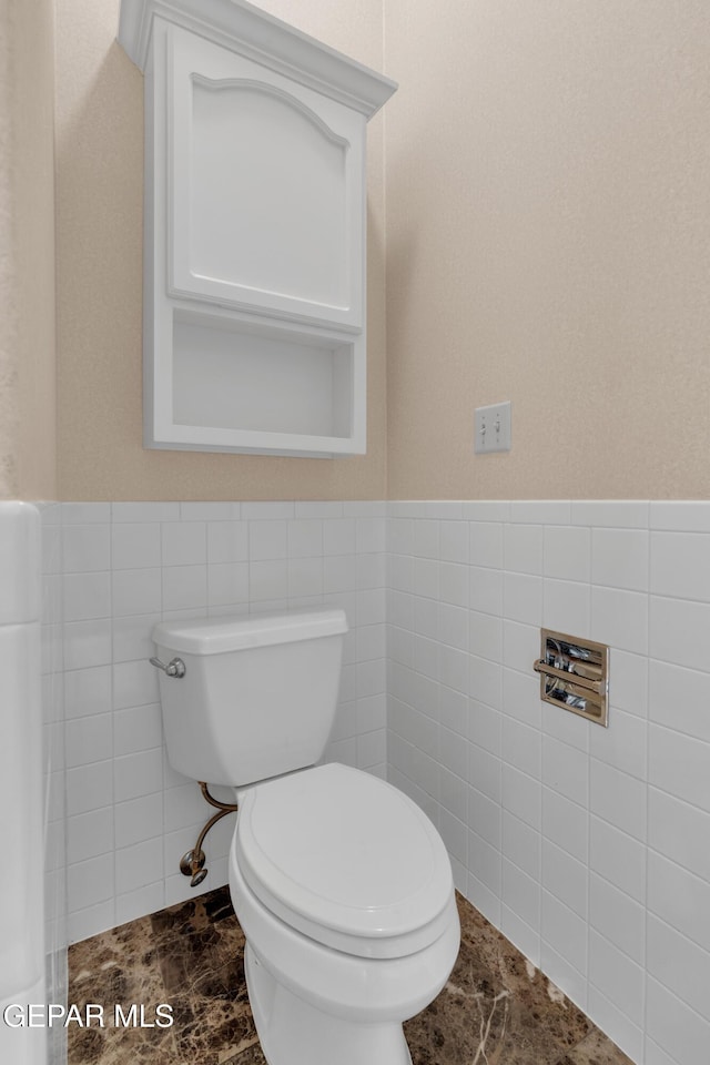 bathroom with tile walls, wainscoting, and toilet