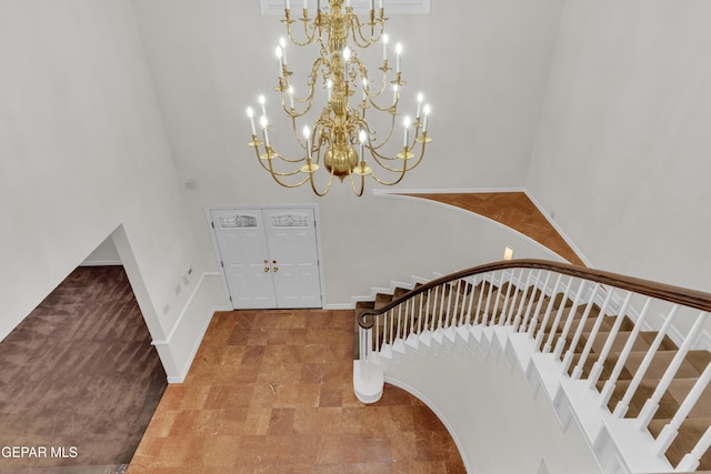 foyer featuring baseboards, a high ceiling, stairs, and a notable chandelier